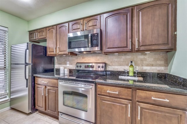 kitchen featuring decorative backsplash, light tile patterned floors, stainless steel appliances, and dark stone countertops