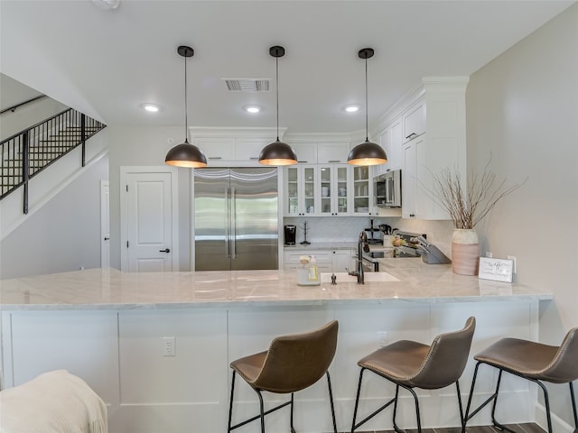 kitchen with white cabinets, kitchen peninsula, decorative light fixtures, stainless steel appliances, and light stone countertops