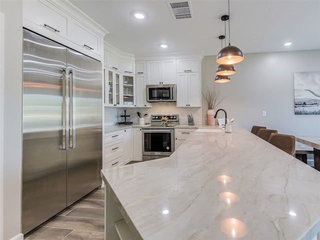 kitchen with white cabinets, hanging light fixtures, sink, appliances with stainless steel finishes, and light stone countertops