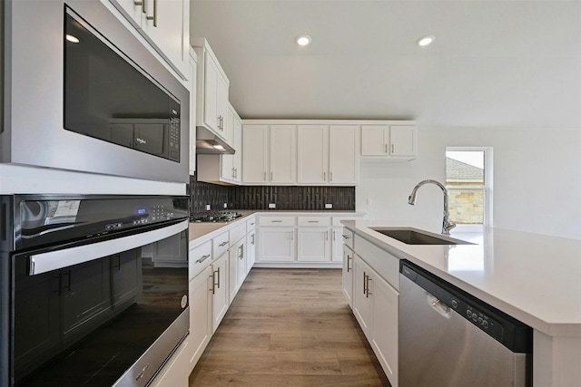 kitchen with light wood-type flooring, white cabinetry, backsplash, appliances with stainless steel finishes, and sink