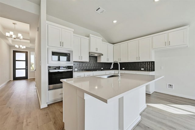 kitchen featuring sink, backsplash, light wood-type flooring, black appliances, and an island with sink