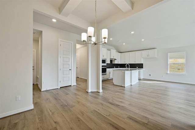 kitchen with decorative light fixtures, backsplash, a center island with sink, light hardwood / wood-style floors, and beamed ceiling