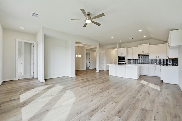 kitchen with light hardwood / wood-style flooring, appliances with stainless steel finishes, tasteful backsplash, ceiling fan, and an island with sink