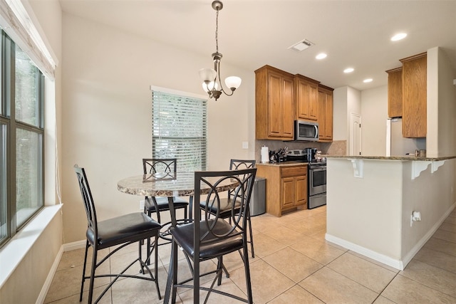 kitchen with decorative light fixtures, a notable chandelier, light tile patterned floors, stainless steel appliances, and light stone counters