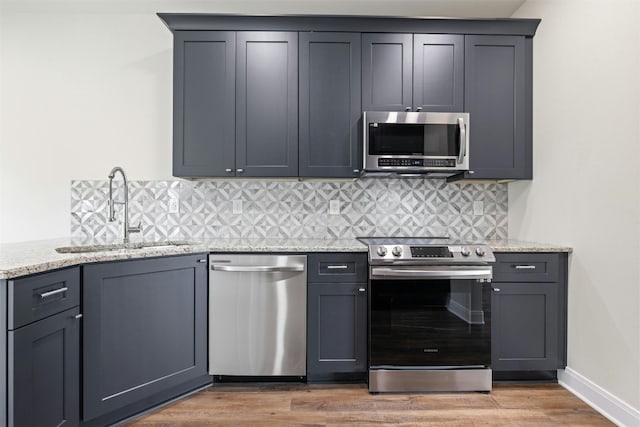 kitchen with stainless steel appliances, tasteful backsplash, hardwood / wood-style floors, light stone counters, and sink