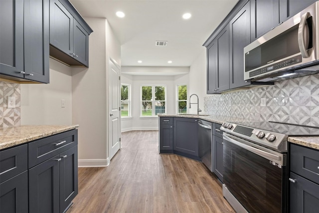 kitchen with appliances with stainless steel finishes, hardwood / wood-style flooring, light stone countertops, backsplash, and sink