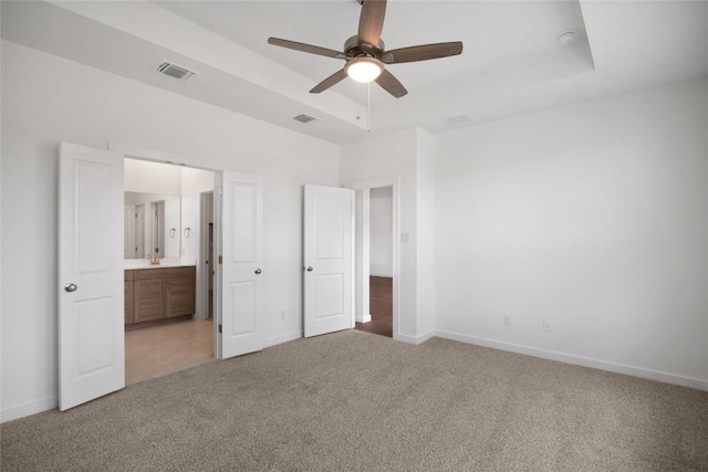 unfurnished bedroom with a raised ceiling, ceiling fan, light colored carpet, and connected bathroom