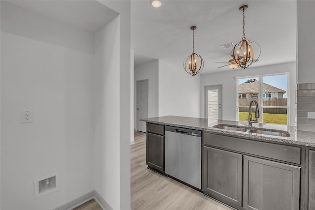 kitchen with hanging light fixtures, sink, stainless steel dishwasher, light stone counters, and light hardwood / wood-style floors