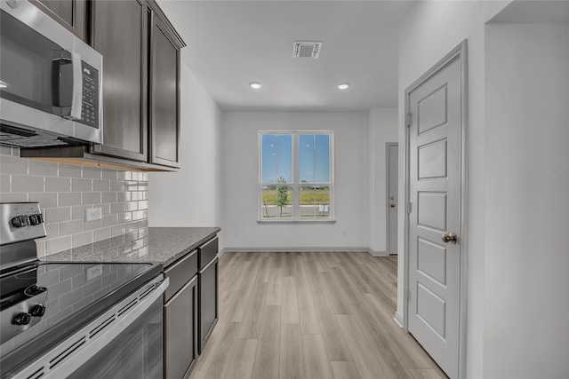 kitchen with tasteful backsplash, appliances with stainless steel finishes, dark stone counters, light hardwood / wood-style flooring, and dark brown cabinetry