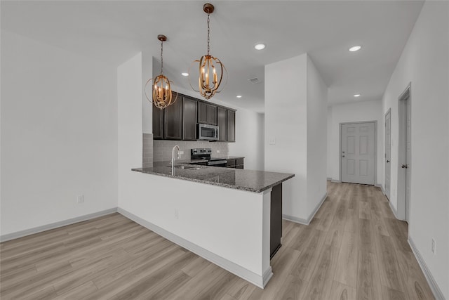 kitchen featuring appliances with stainless steel finishes, kitchen peninsula, dark stone countertops, and light hardwood / wood-style floors