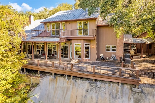 back of house with a balcony, a standing seam roof, a chimney, central air condition unit, and metal roof