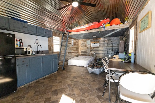 kitchen featuring black refrigerator, ceiling fan, sink, wood walls, and blue cabinetry