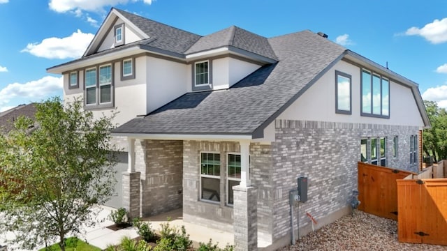 exterior space featuring stucco siding, a gate, fence, roof with shingles, and brick siding