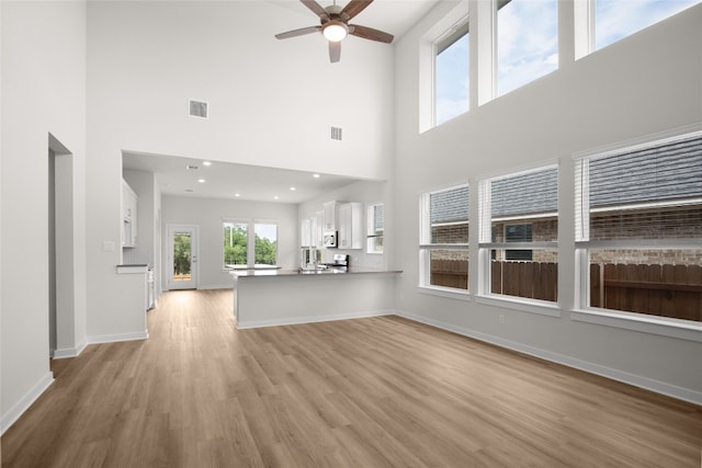 unfurnished living room featuring light wood-type flooring, a towering ceiling, and ceiling fan