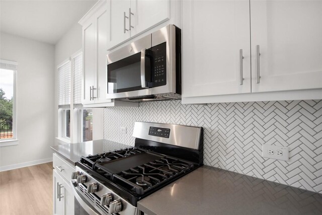 kitchen featuring light wood-type flooring, dark countertops, stainless steel appliances, white cabinets, and decorative backsplash