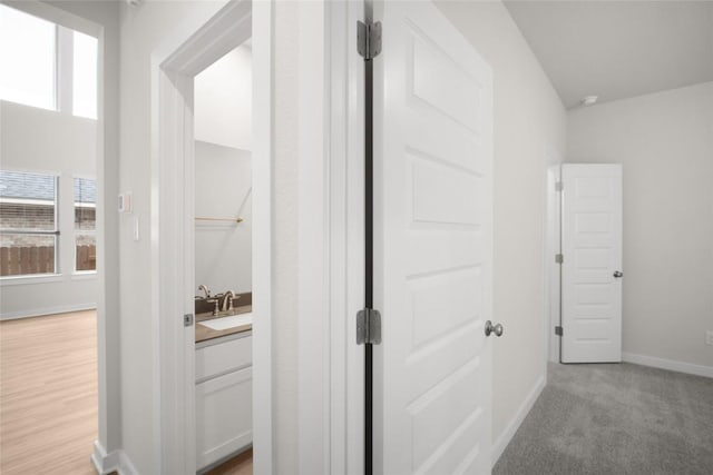 hall featuring baseboards and light colored carpet