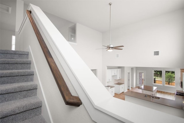 stairway with wood finished floors, a high ceiling, a ceiling fan, and visible vents