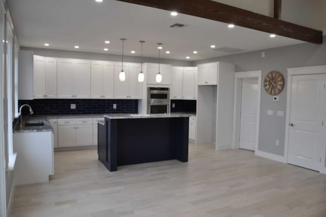 kitchen featuring double oven, light wood-type flooring, white cabinets, and a center island