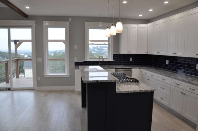 kitchen with pendant lighting, light stone counters, a kitchen island, light hardwood / wood-style floors, and white cabinetry