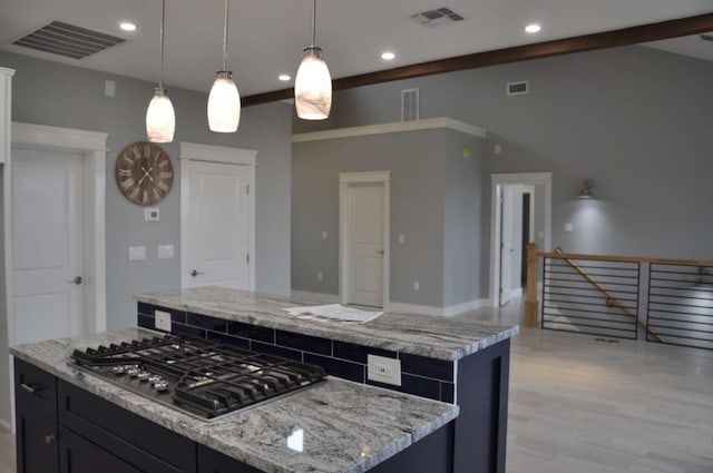 kitchen with pendant lighting, light wood-type flooring, a center island, light stone countertops, and stainless steel gas stovetop