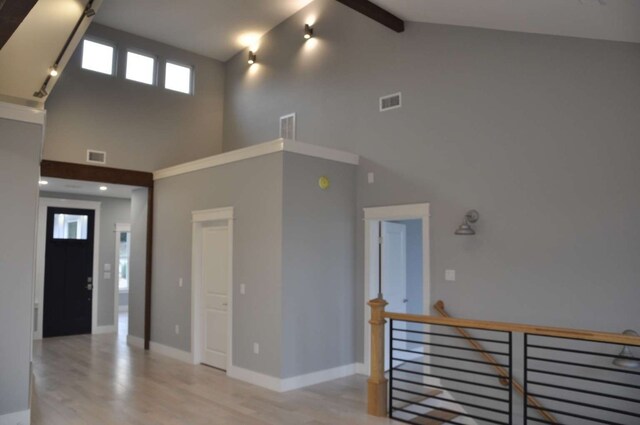 hallway with light wood-type flooring, beamed ceiling, high vaulted ceiling, and a healthy amount of sunlight