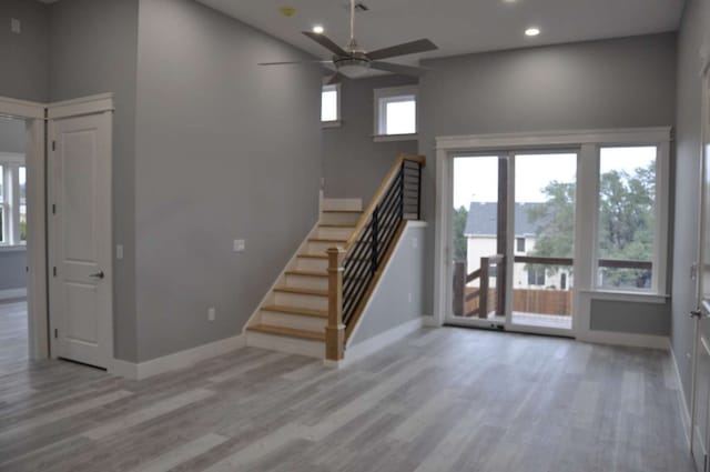 stairway with a towering ceiling, a healthy amount of sunlight, ceiling fan, and light hardwood / wood-style flooring