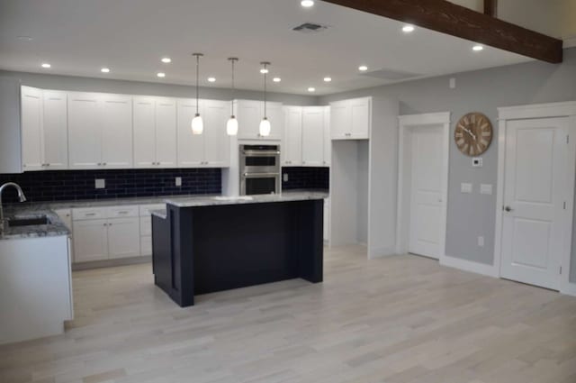 kitchen with white cabinets, double oven, a center island, and light hardwood / wood-style floors