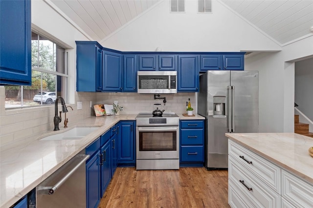 kitchen featuring appliances with stainless steel finishes, light wood-type flooring, backsplash, sink, and vaulted ceiling