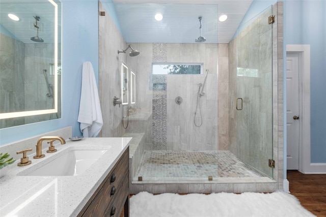 bathroom featuring a shower with door, vaulted ceiling, hardwood / wood-style floors, and vanity with extensive cabinet space