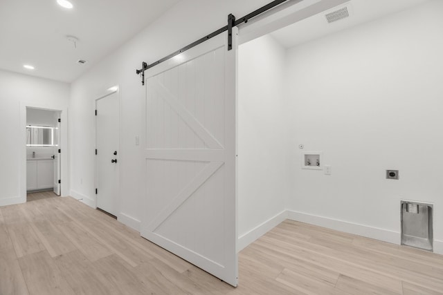 clothes washing area featuring electric dryer hookup, a barn door, light hardwood / wood-style floors, and hookup for a washing machine