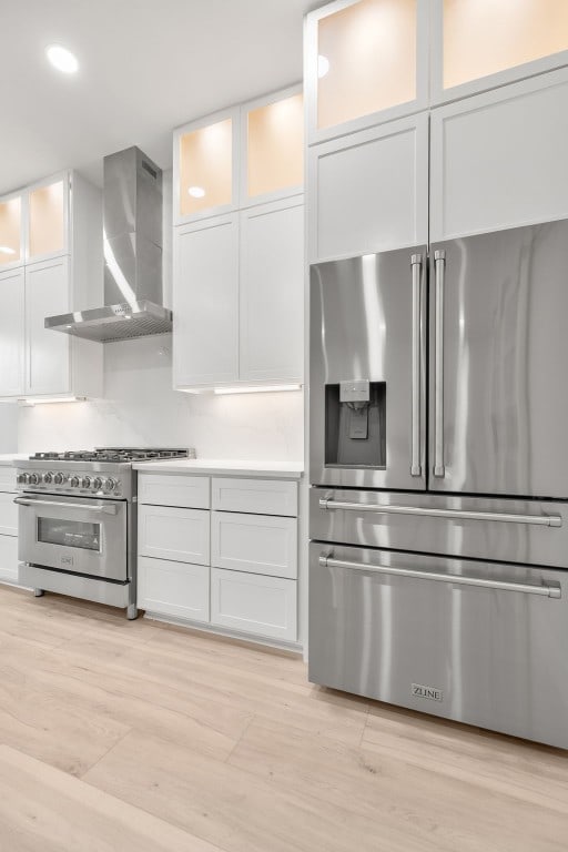 kitchen featuring wall chimney exhaust hood, white cabinetry, appliances with stainless steel finishes, and light hardwood / wood-style flooring