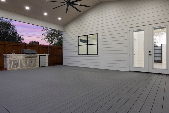 deck at dusk featuring area for grilling, an outdoor kitchen, and ceiling fan