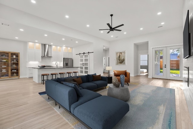 living room featuring a barn door, ceiling fan, light hardwood / wood-style floors, and french doors