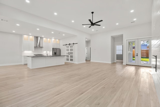 unfurnished living room featuring ceiling fan, light wood-type flooring, a barn door, and french doors