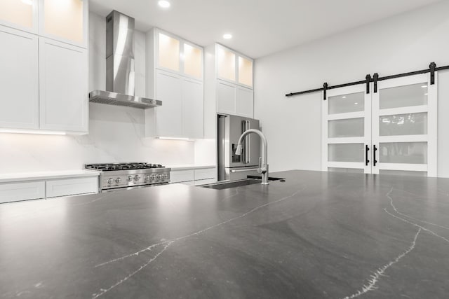 interior space featuring sink, premium appliances, wall chimney range hood, a barn door, and white cabinetry