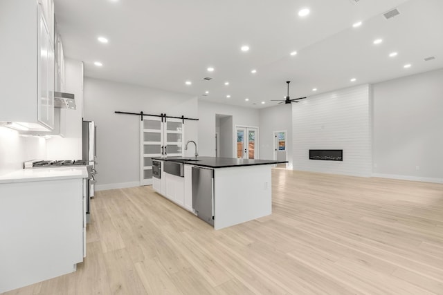 kitchen with appliances with stainless steel finishes, a fireplace, a barn door, white cabinetry, and light wood-type flooring