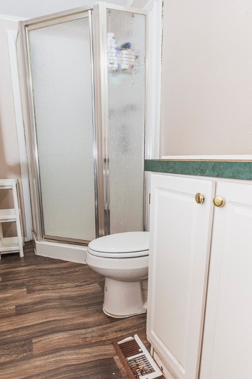 bathroom with an enclosed shower, toilet, and wood-type flooring