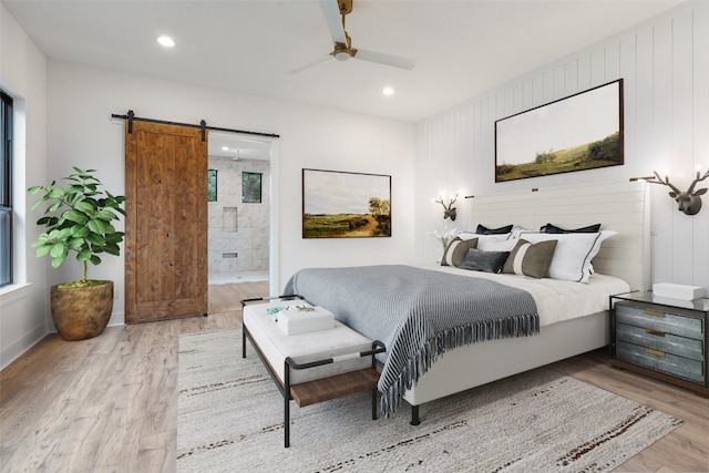 bedroom with connected bathroom, light hardwood / wood-style floors, ceiling fan, and a barn door