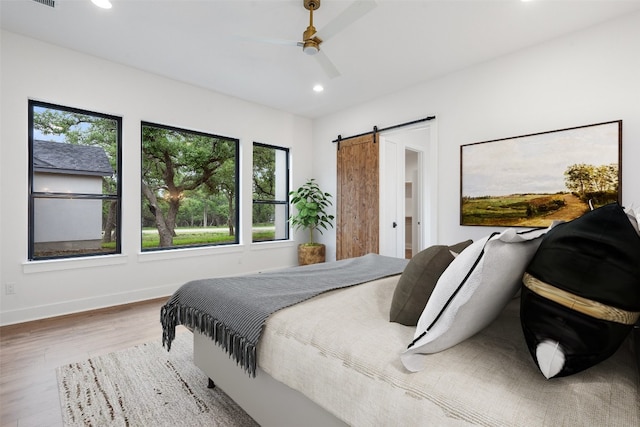 bedroom with wood-type flooring, ceiling fan, and a barn door