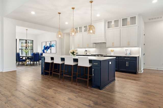 kitchen with hanging light fixtures, an island with sink, white cabinetry, dark hardwood / wood-style flooring, and a breakfast bar