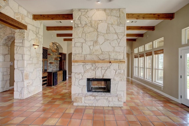 unfurnished living room with arched walkways, a fireplace, beam ceiling, and tile patterned floors