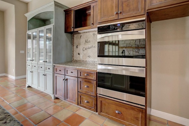 kitchen with light tile patterned floors, stainless steel double oven, backsplash, and baseboards