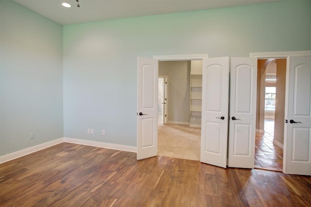 unfurnished bedroom featuring arched walkways, baseboards, and wood finished floors