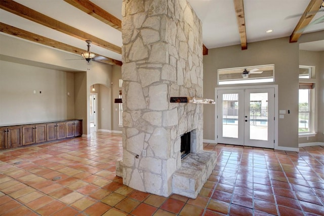 unfurnished living room with a fireplace, light tile patterned floors, ceiling fan, beam ceiling, and french doors