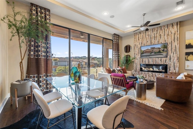 dining area featuring a tray ceiling, recessed lighting, visible vents, a glass covered fireplace, and wood finished floors