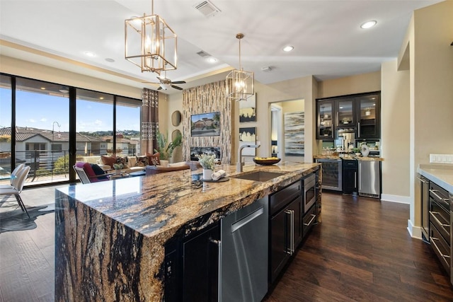 kitchen featuring a kitchen island with sink, a sink, visible vents, light stone countertops, and glass insert cabinets