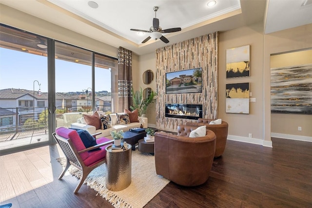 living room with baseboards, a ceiling fan, wood finished floors, a tray ceiling, and a fireplace