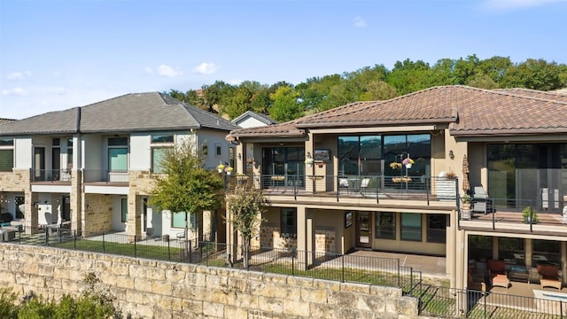 rear view of house with a tiled roof, fence, and stucco siding