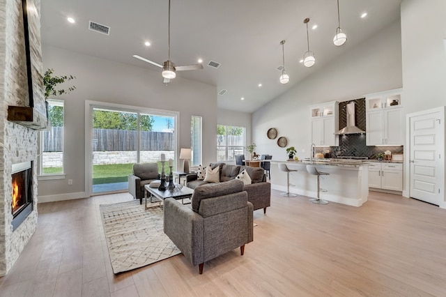 living room with light wood-type flooring, ceiling fan, sink, high vaulted ceiling, and a fireplace