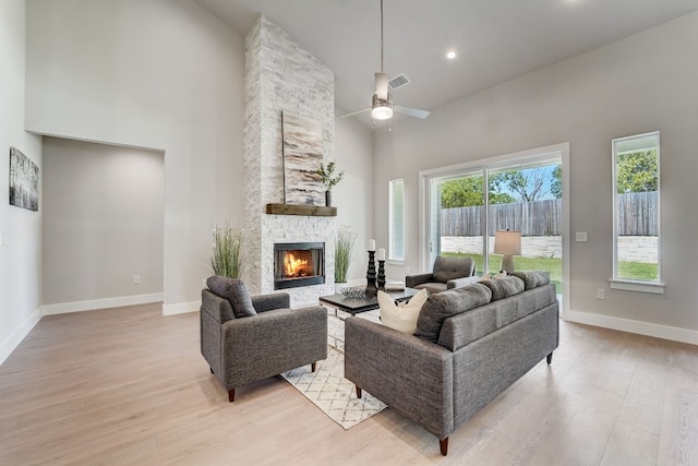 living room with a stone fireplace, ceiling fan, light hardwood / wood-style flooring, and a high ceiling